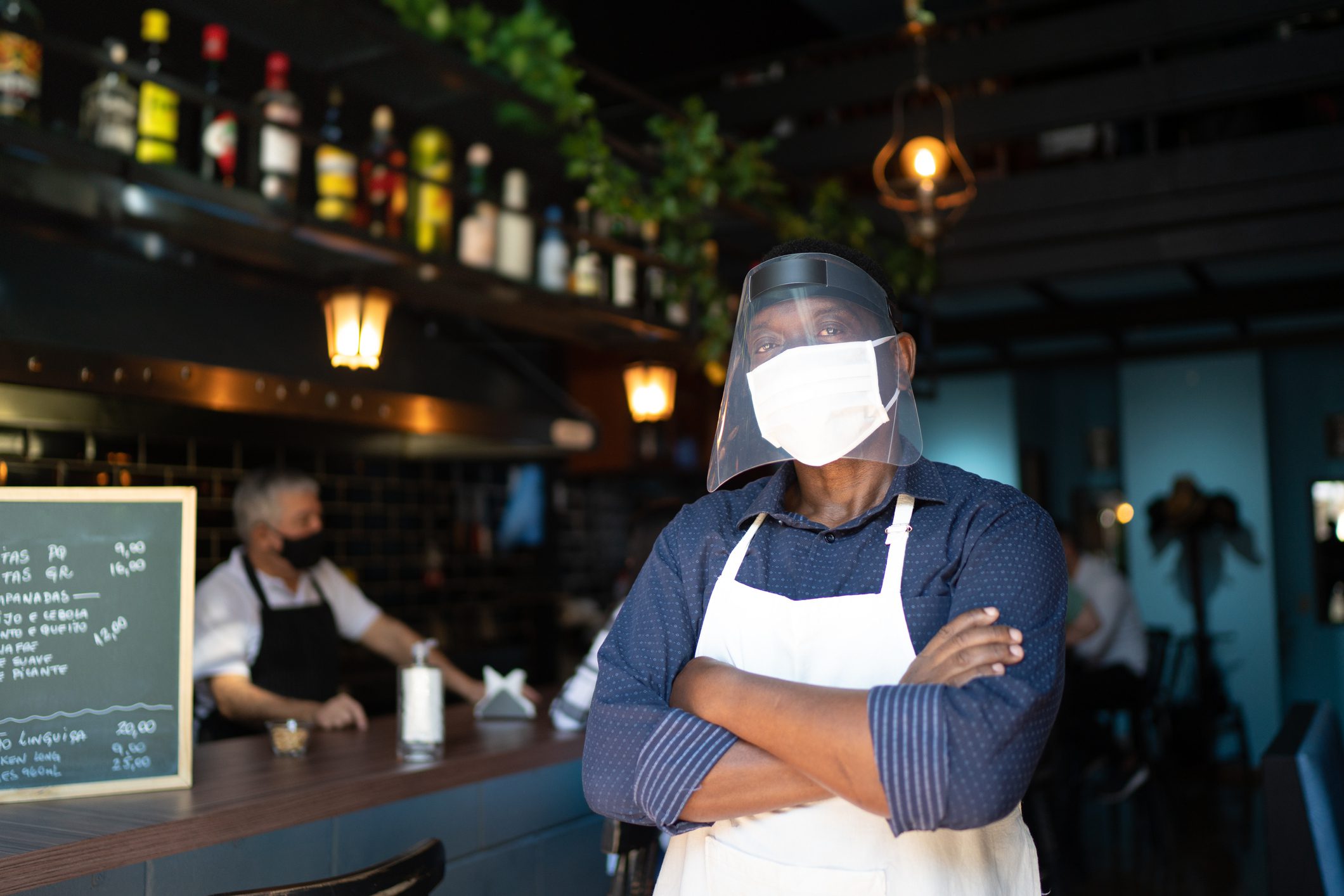 Portrait of a waiter with arms crossed and wearing protective face mask at restaurant
