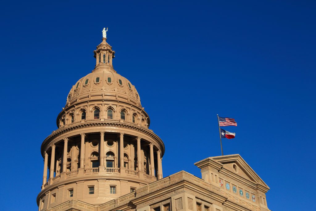 Texas State Capitol with a flag on a clear blue sky