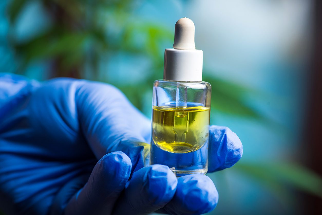 Scientist holding cannabis marijuana oil in a small jar close up
