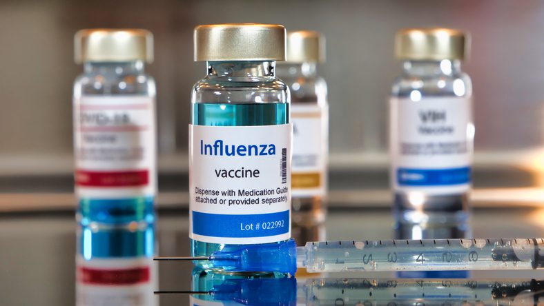 Bottles of influenza vaccine. ottles with a syringe on black table and stainless steel background.