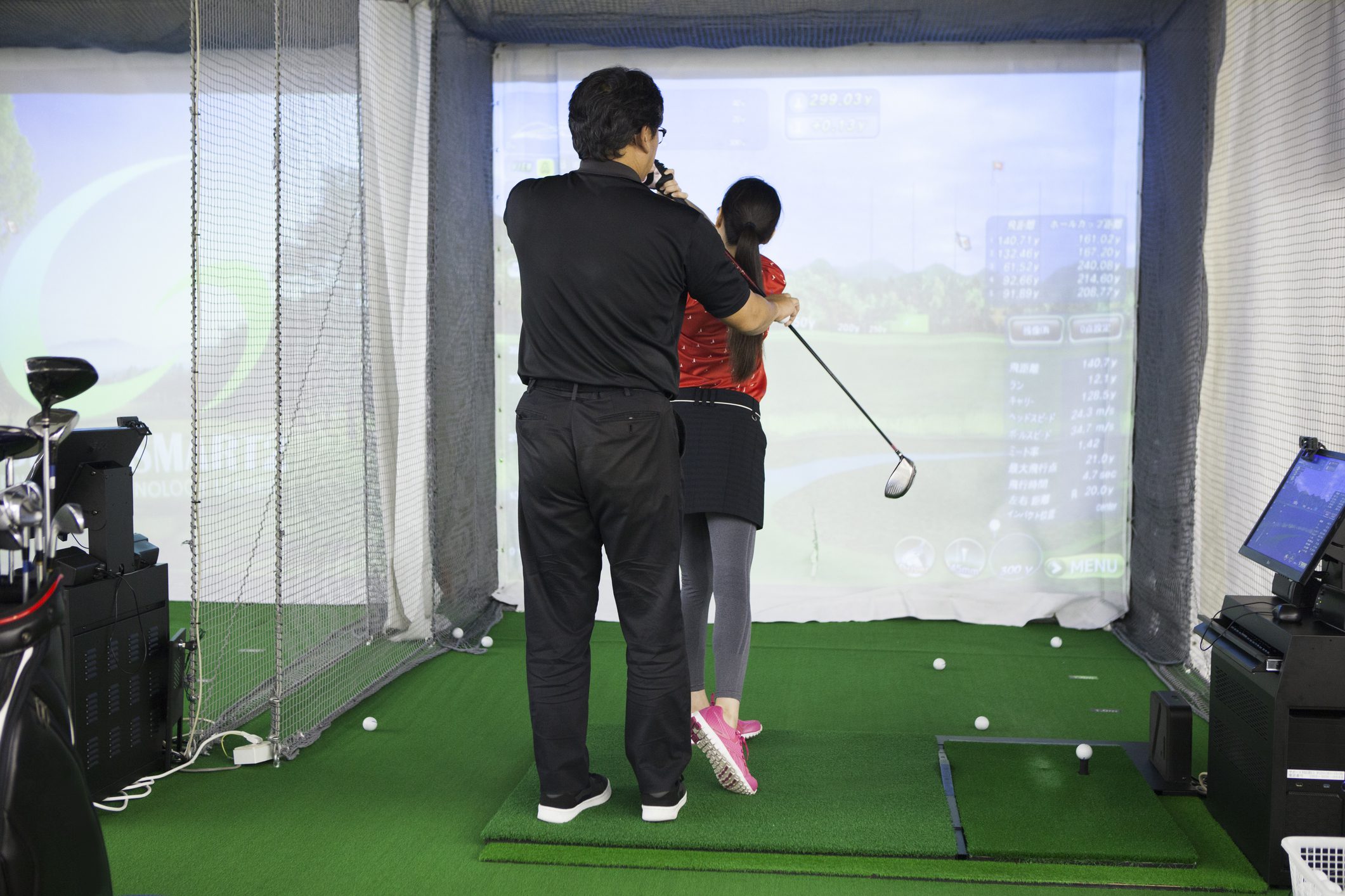 Una mujer practicando en un estudio de golf y un hombre con un entrenador.
