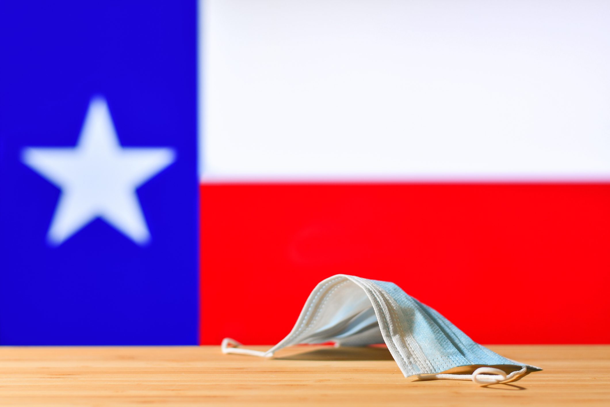 A medical mask lies on the table against the background of the flag of Texas.