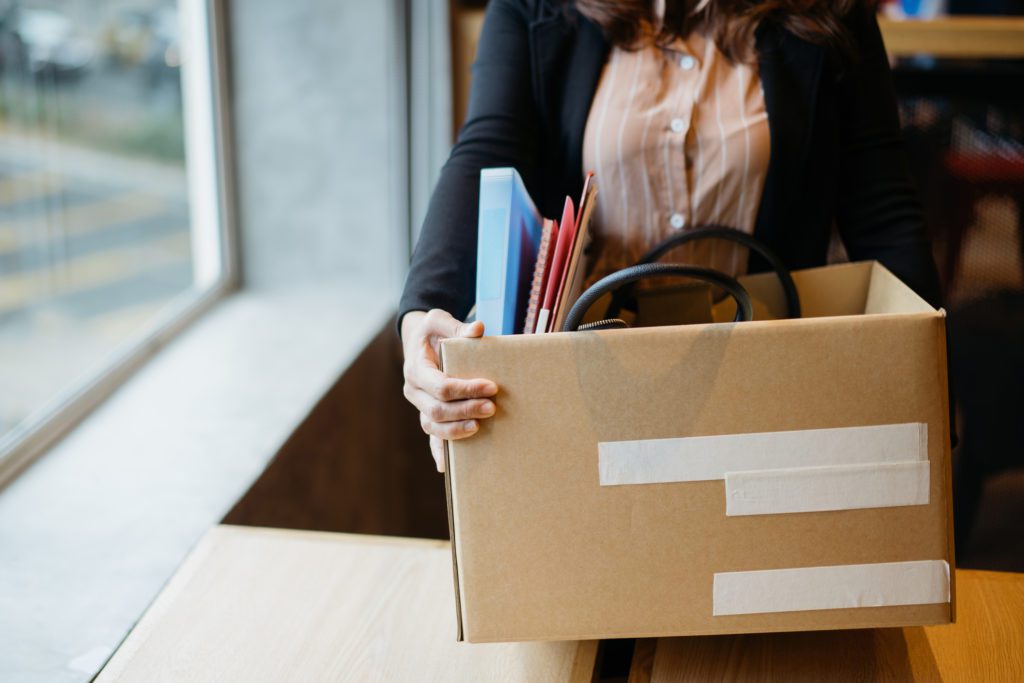 Asian woman holding cardboard box containing personal belongings looking for new job