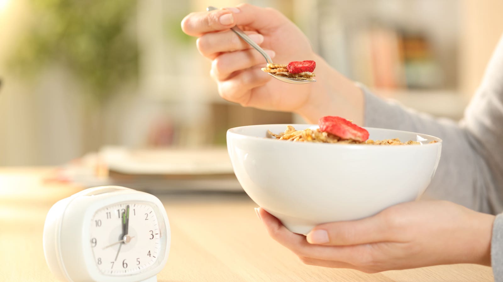 Close-up of woman's hands eating cereal bowl with fruit after intermittent fasting sitting on a table at home. | Image by Pheelings Media, Shutterstock