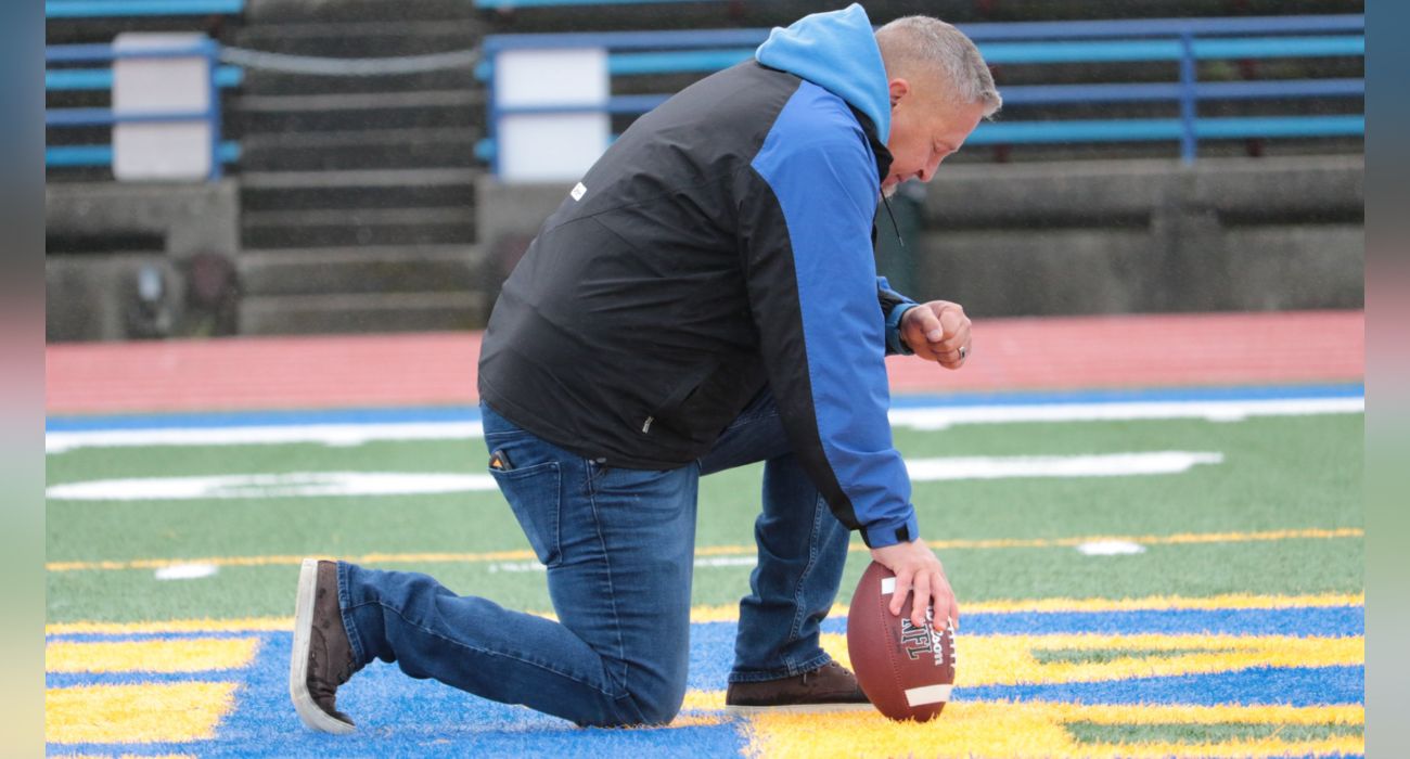 Joseph Kennedy kneels on a football field