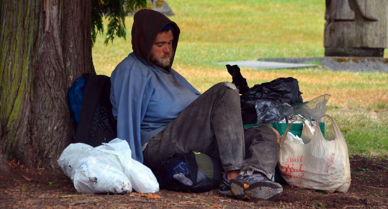 Homeless man sits next to a tree