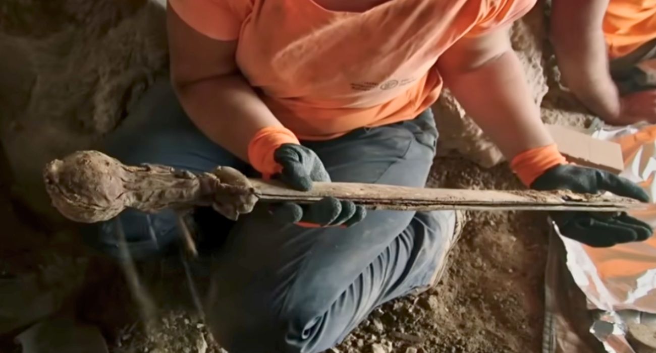 an archaeologist retrieving a sword from a cave
