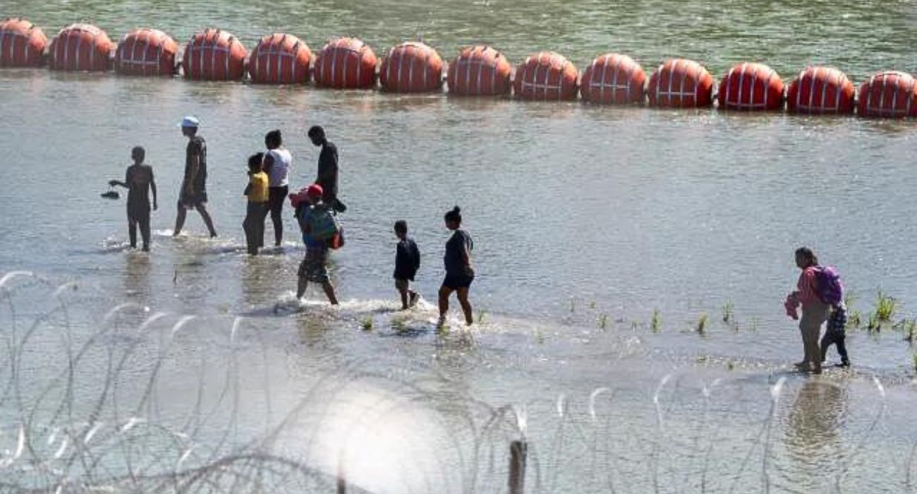 Unlawful migrants walk by a string of buoys