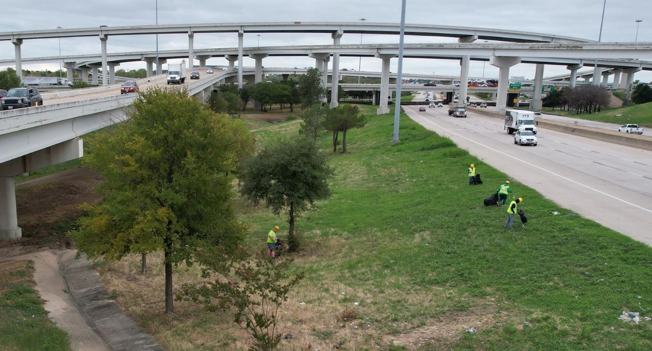 UpSpire crews collect litter in a grassy median beside a Fort Worth highway.