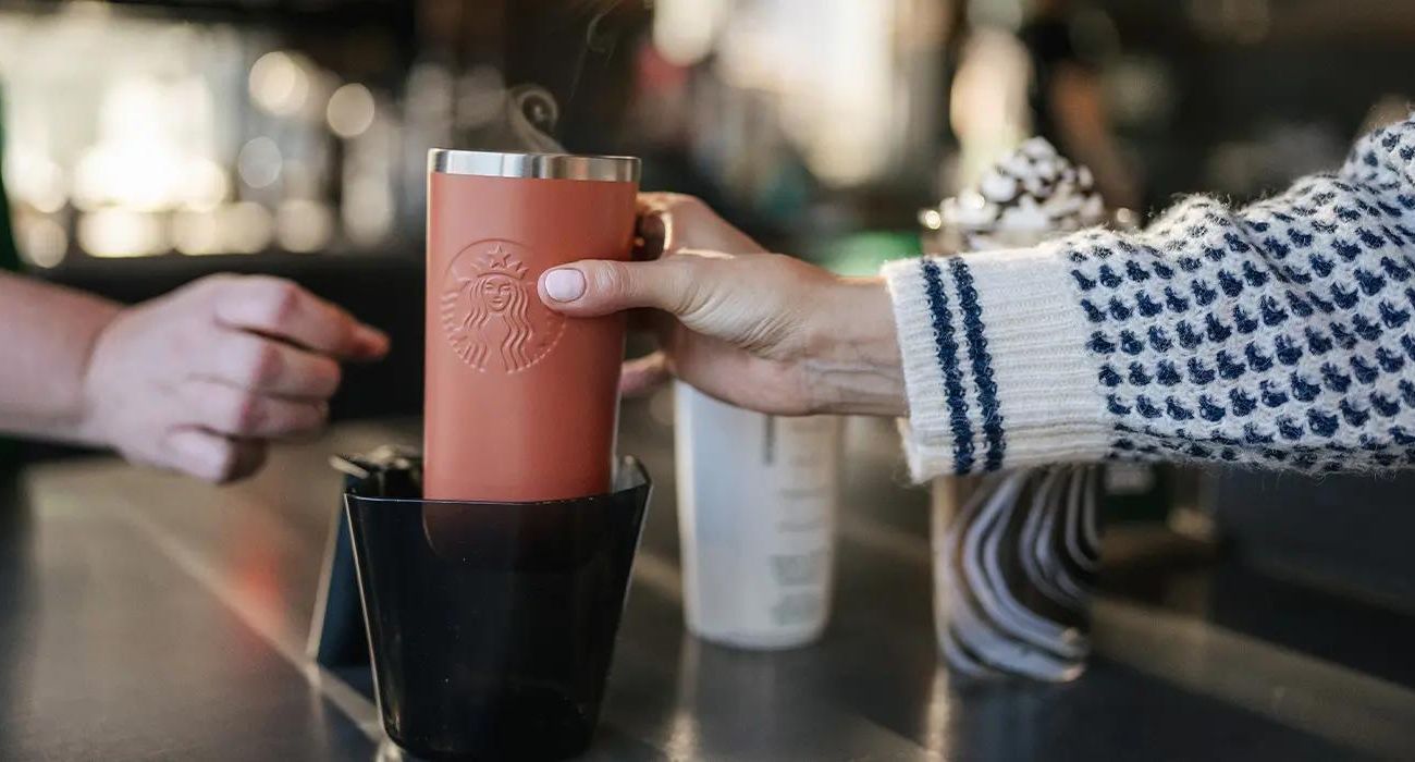 Starbucks customer puts personal cup in container for worker to use.