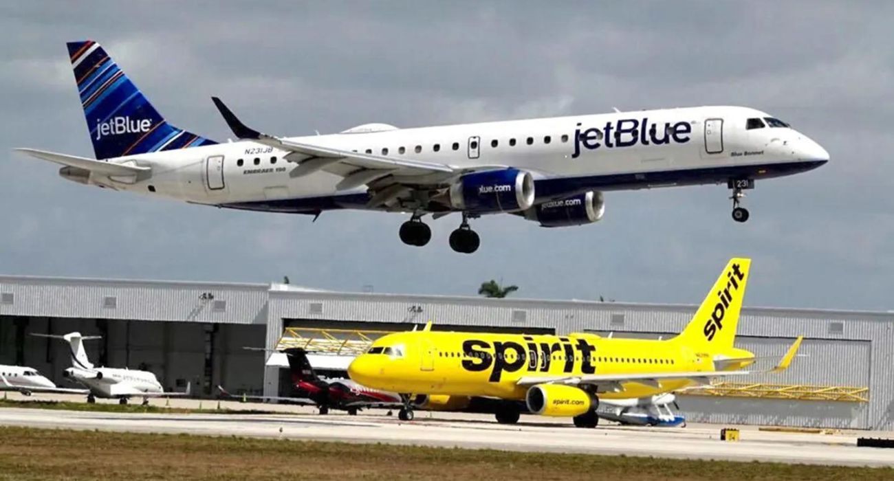 A JetBlue airliner lands past a Spirit Airlines jet on taxi way.