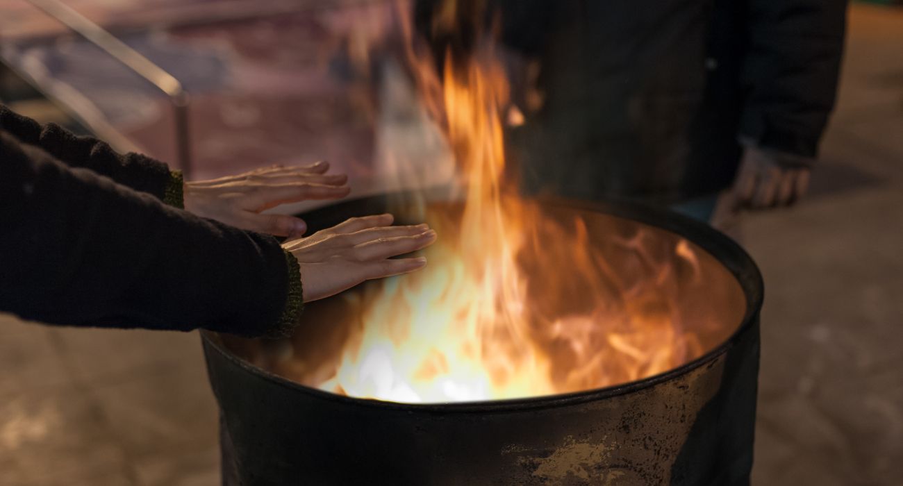 Hombre sin hogar calentándose las manos con fuego de barril