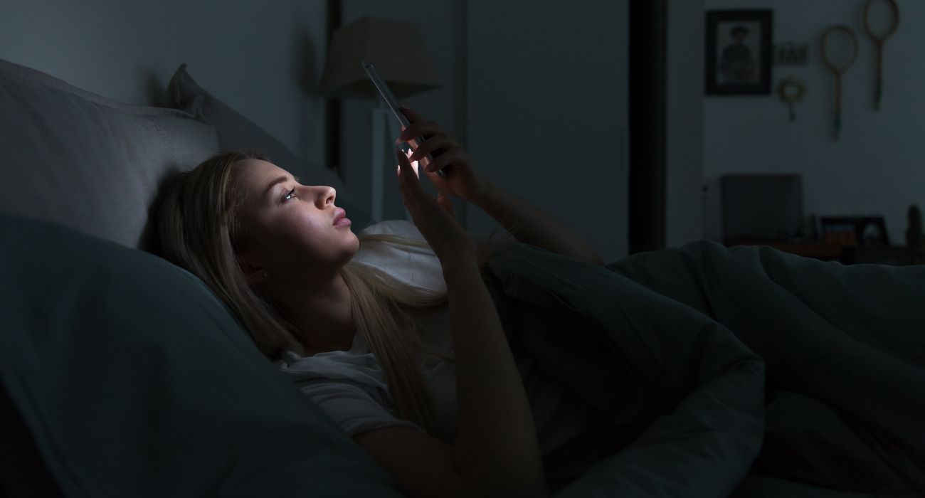 Young woman on phone in bed | Image by DimaBerlin/Shutterstock