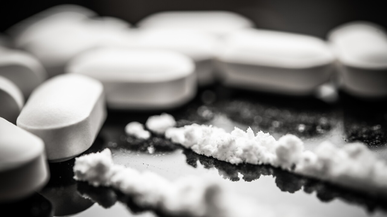 Stock image depicting opioid pills and powdered fentanyl on a dark surface